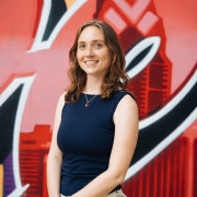 Image of artist standing in front of a painted mural of Philadelphia's skyline. 