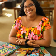 Alyssa Reynoso-Morris sitting and smiling with her books displayed on a table in front of her.