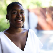 a headshot of a bald Black woman in a white top smiling widely. 