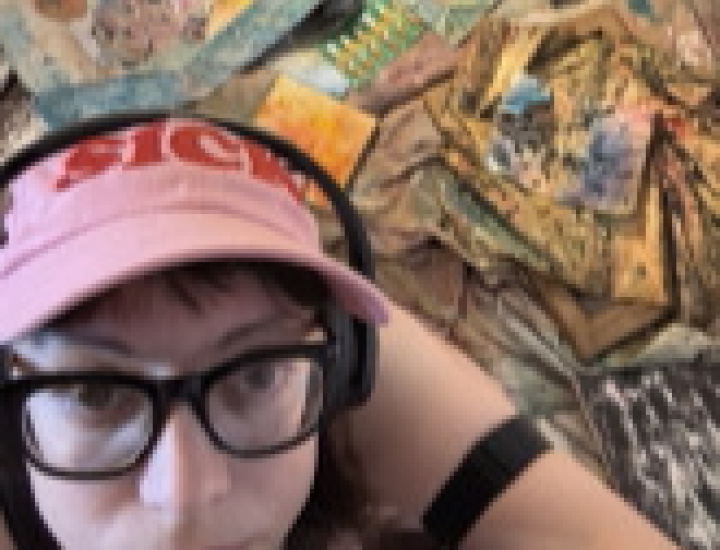 46 year old female identifying person wearing a pink hat with "sick" embroidered on it in red. In the background, colorful sculpted paintings are strewn over the ground.
